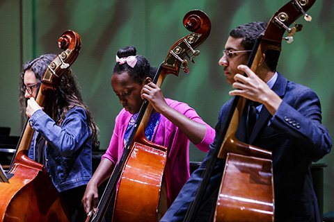 Three musicians from the Shalala Music Outreach program are performing with cellos on stage 