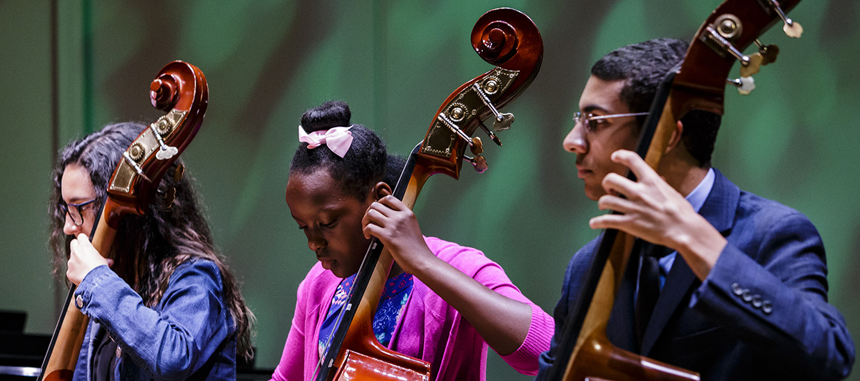 Three musicians from the Shalala Music Outreach program are performing with cellos on stage 