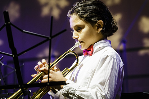 A musician wearing a white dress shirt with red bow-tie plays the trumpet